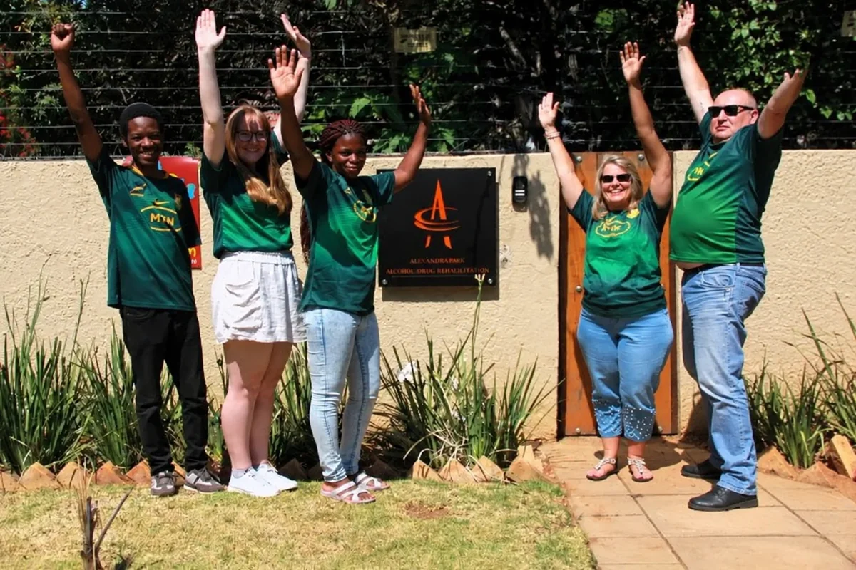 A group gathered outdoors at Alexandra Park with raised arms, wearing South African rugby jerseys